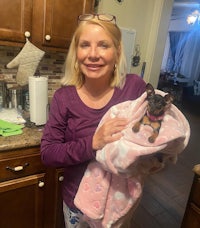 a woman holding a small dog in a pink blanket