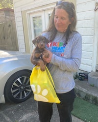 a woman holding a puppy in a yellow bag