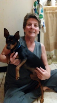 a woman holding a black and tan dog in a kitchen