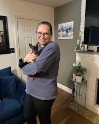 a woman holding a dog in front of a fireplace